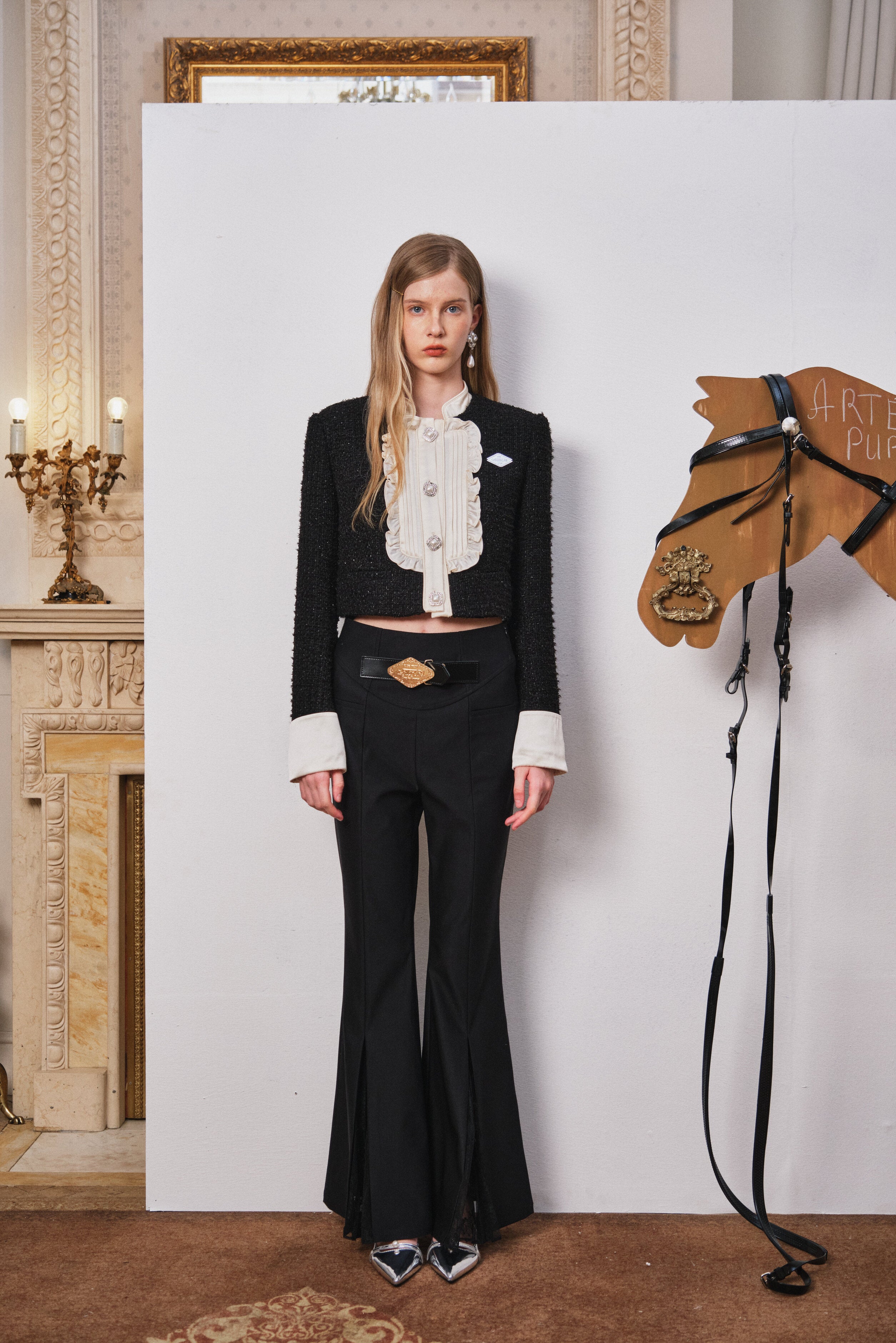 Woman in a black outfit standing next to a wooden horse model in an elegant interior setting.