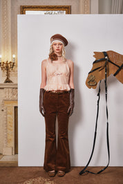 Woman in vintage outfit with horse head sculpture and bridle against a white wall.